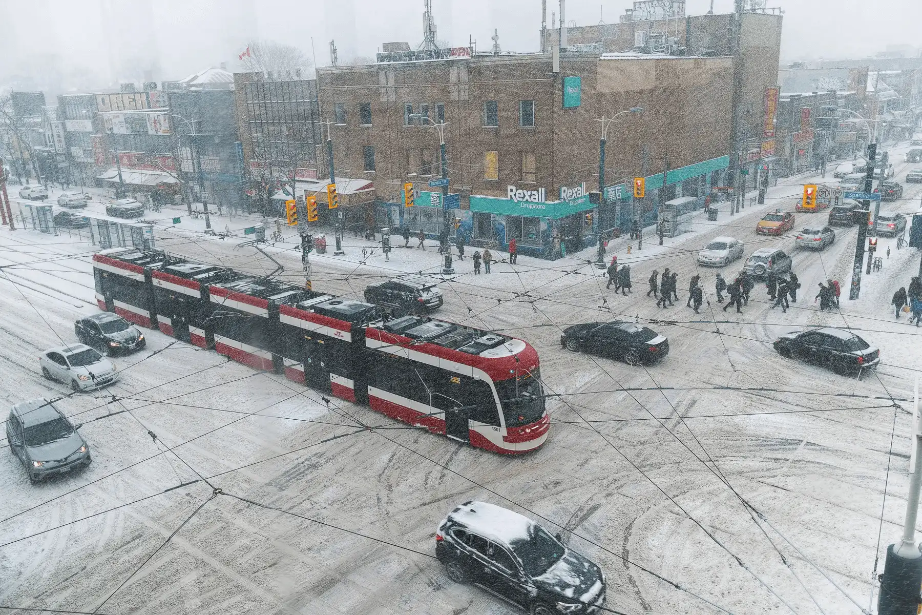 Snow-covered Toronto streets with pedestrians and streetcars navigating through a winter storm.