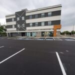 Freshly paved commercial parking lot with newly painted accessible parking spaces in front of a modern three-story office building.