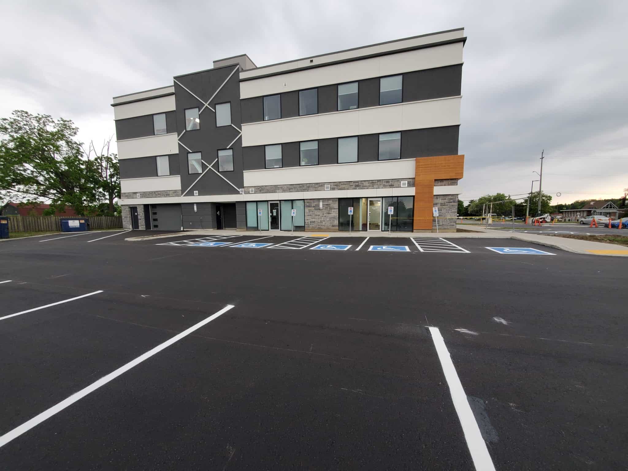 Freshly paved commercial parking lot with newly painted accessible parking spaces in front of a modern three-story office building.