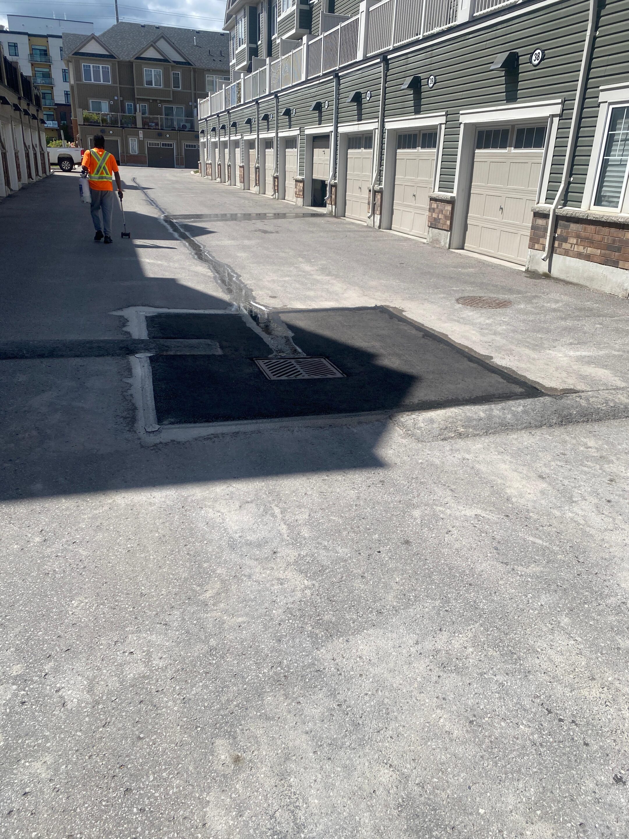 Worker applying sealant to freshly repaired asphalt patches around a drainage system in a residential townhouse complex, ensuring durability and water protection.