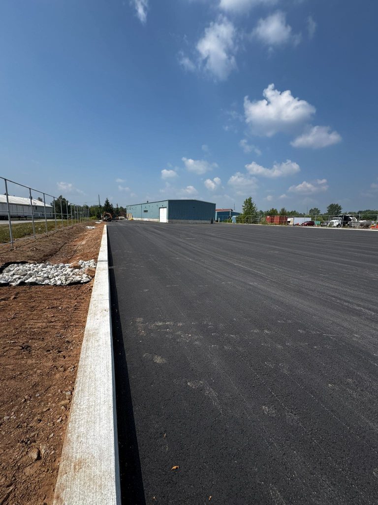 Empire Paving completing a commercial roadway paving project in Markham featuring freshly laid asphalt, new concrete curbs, and clear skies overhead.
