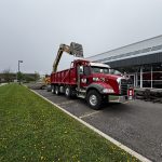 Empire Paving red dump truck parked in a commercial parking lot in Ontario while an excavator loads removed asphalt into the truck during parking lot reconstruction.