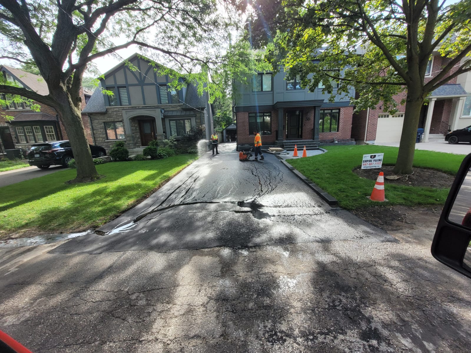 Why Some Driveways Fail Within 5 Years Residential driveway undergoing asphalt maintenance with workers applying sealcoating and preparing the surface in a suburban neighborhood.