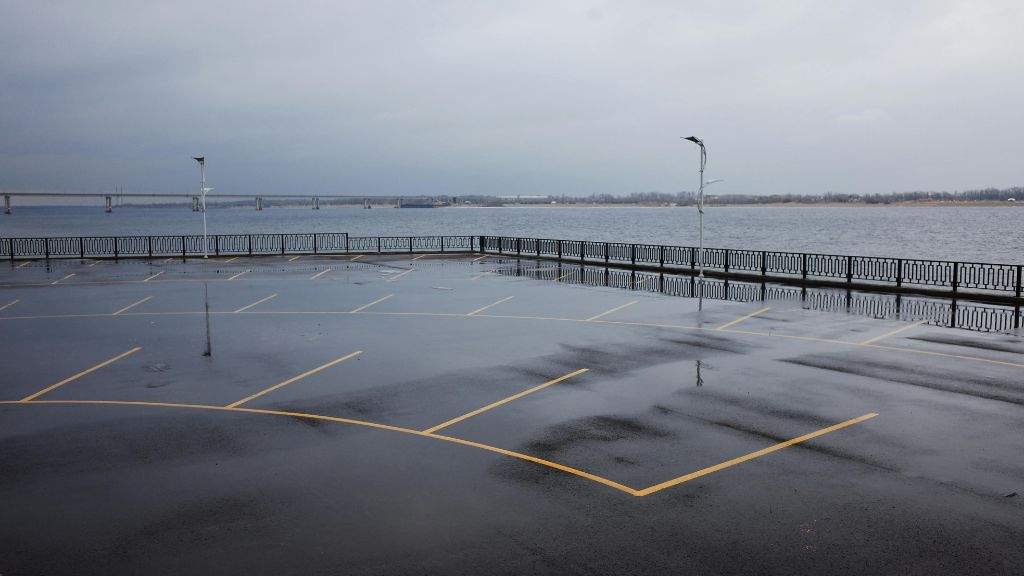 BLOG 1 Wet commercial asphalt parking lot along a waterfront railing showing water accumulation from trapped organic debris.